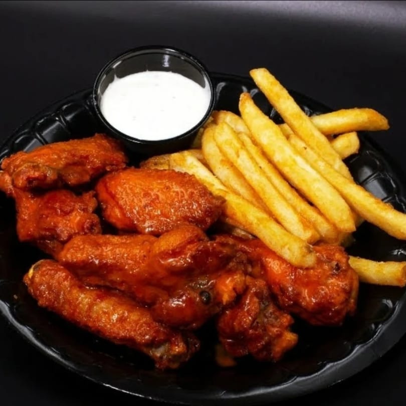Spicy chicken wings with golden french fries and a side of ranch dressing on a black plate.