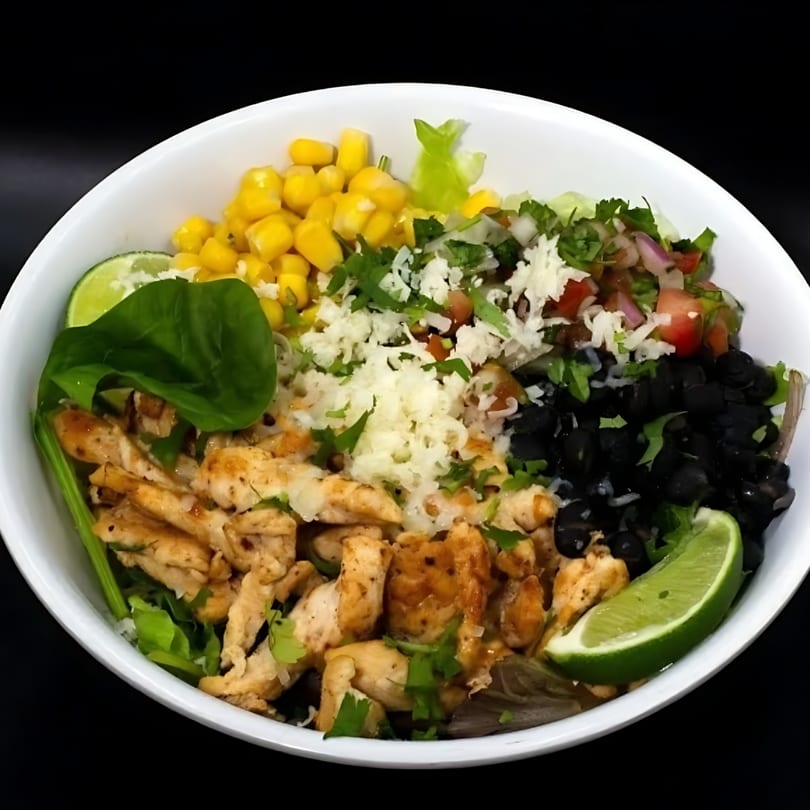 Mexican chicken bowl with corn, black beans, pico de gallo, cheese, and lime wedges.